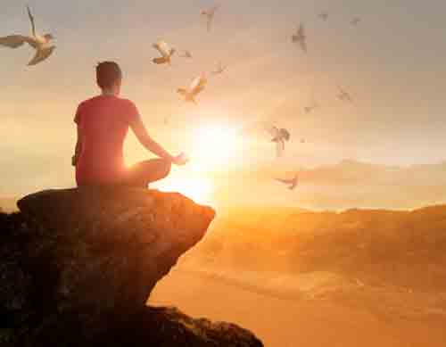 A person meditating on the edge of a cliff in front of a beautiful sunset surrounded by beautiful flying doves.